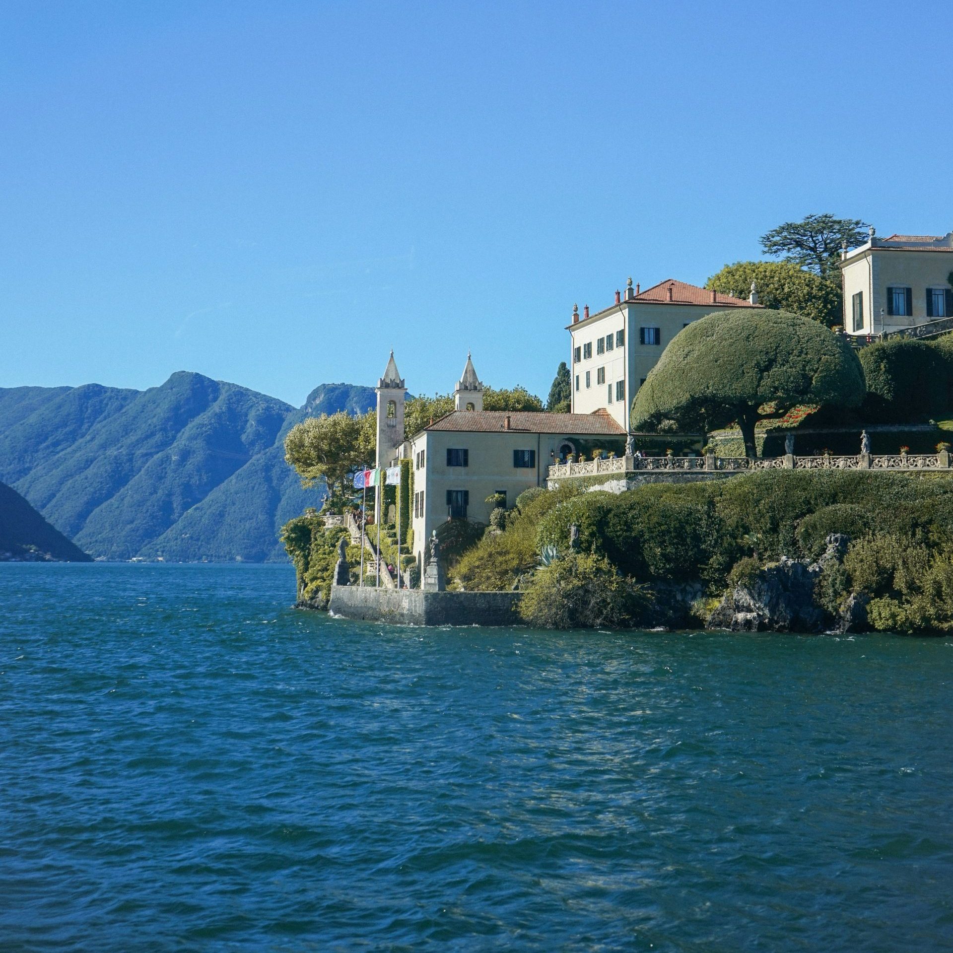 Elegant villas on a hillside overlooking a blue lake.